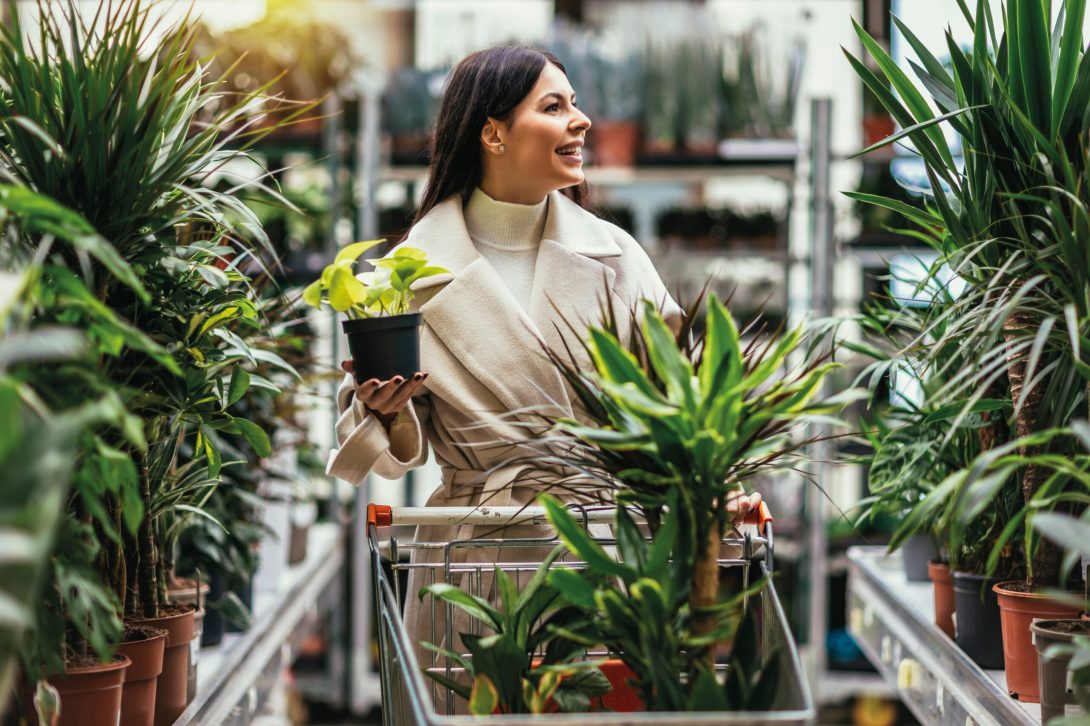 Woman buying flowers pushing shopping cart in garden center.